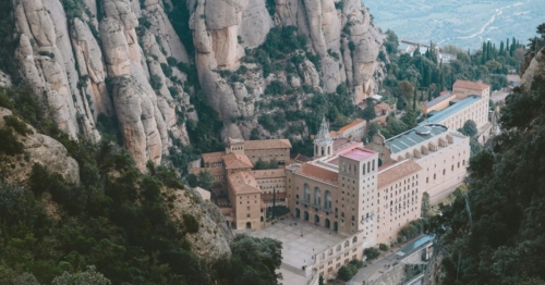 View of a monastery and basilica that are at the base of steep rocky mountains.